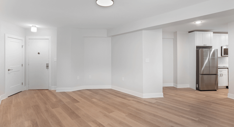 an empty living room with white walls and a stainless steel refrigerator